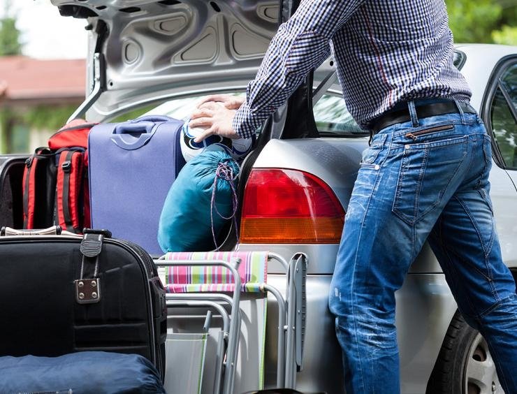 um homem a colocar bagagem no porta-bagagens de um carro